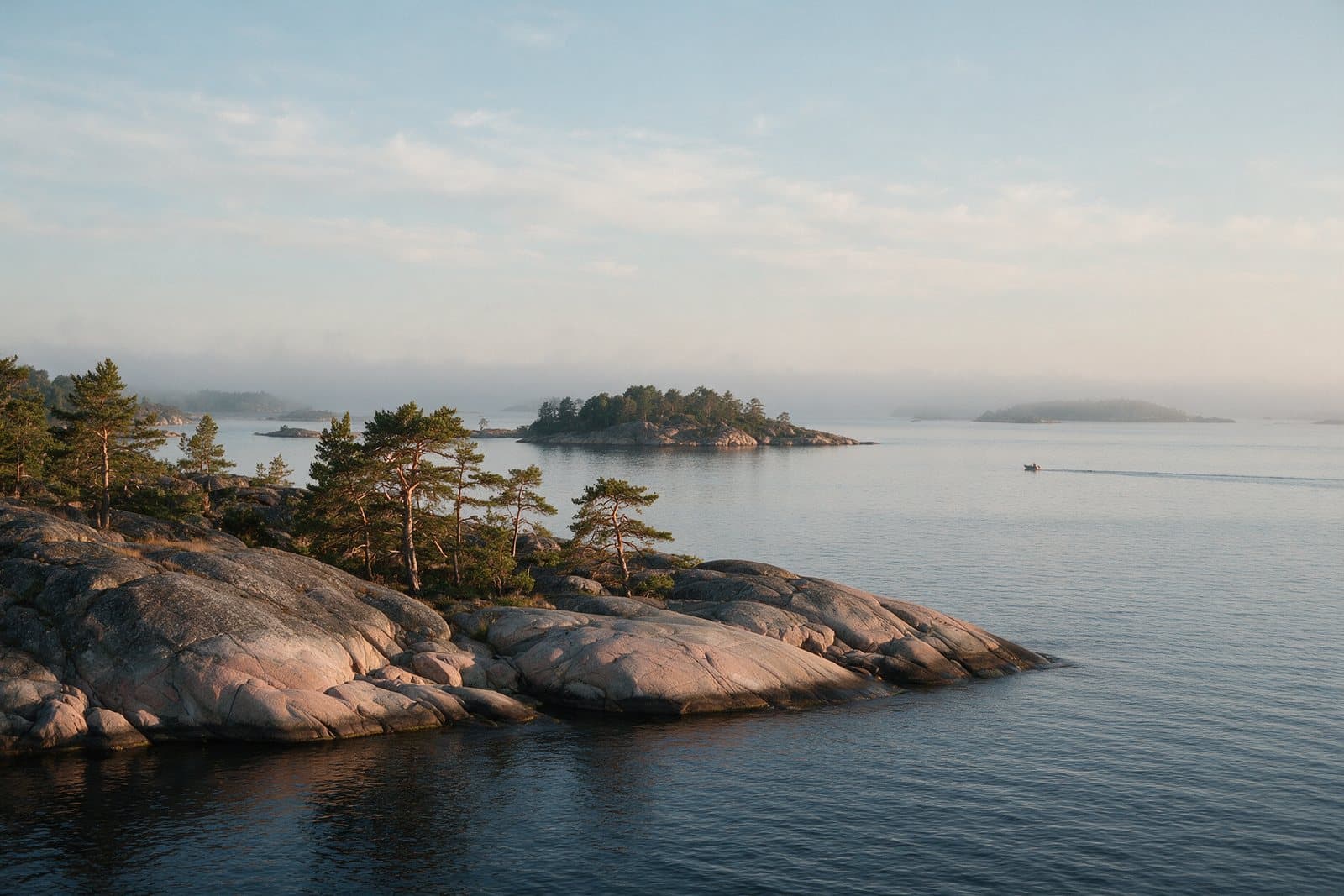Klippor, tallar och öar i Stockholms skärgård med en båt långt ute på fjärden